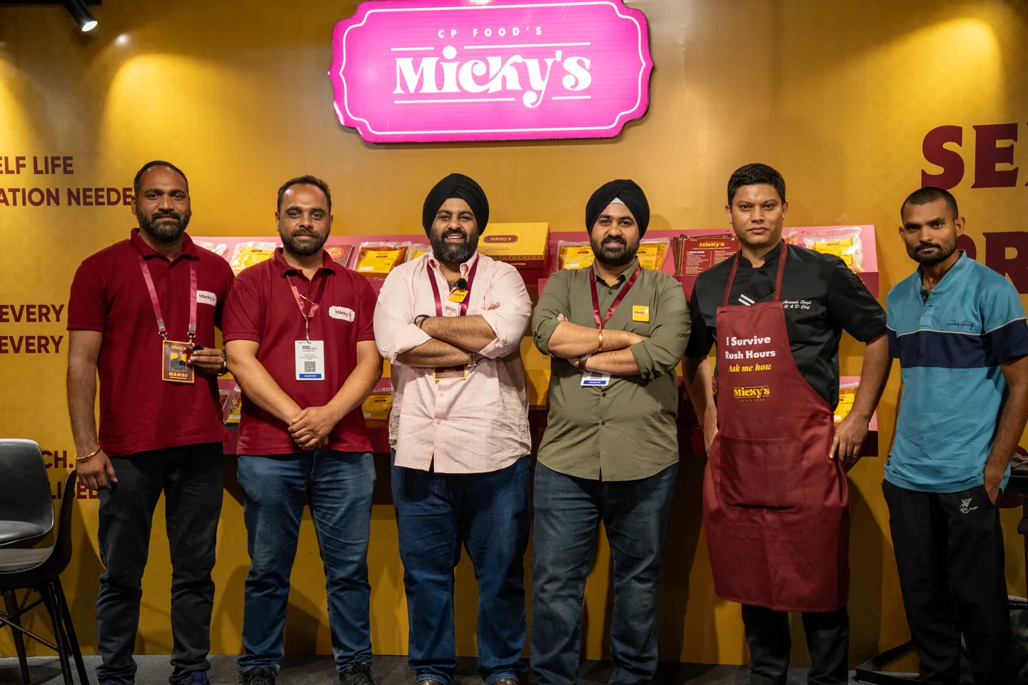 The Micky’s team at the booth, one in the maroon “I Survive Rush Hours” apron, under the pink Micky’s sign