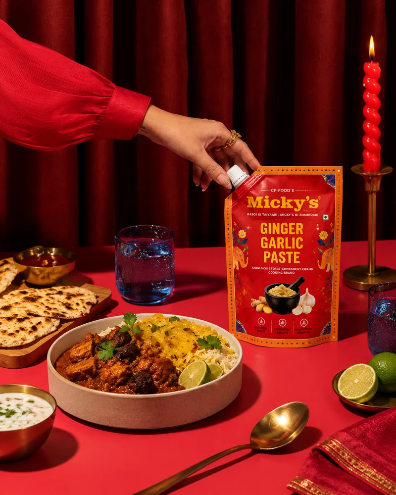 A hand opening a Micky’s Ginger Garlic Paste spout pouch on a red table